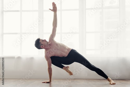 Young man practicing side plank yoga pose