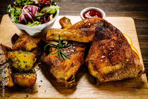 Grilled chicken legs with baked potatoes and vegetable salad on wooden table
