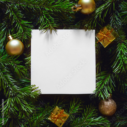 Empty paper blank and golden decorations laying on Christmas tree branches. New year background.