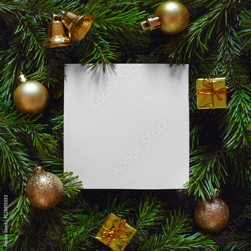 Empty paper blank and golden decorations laying on Christmas tree branches. New year background.