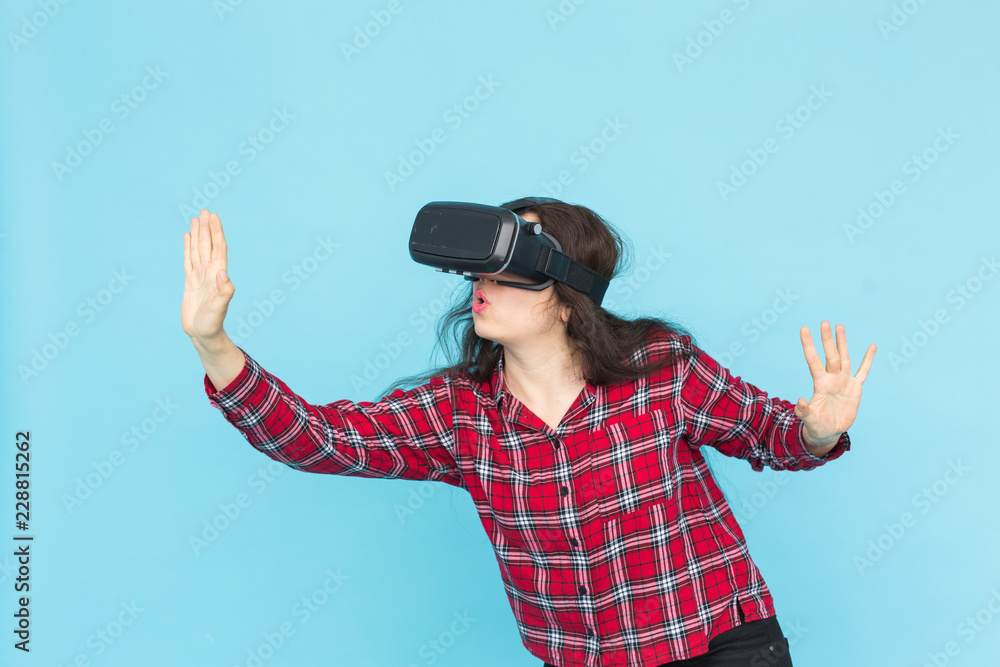 Technology and people concept - Young woman testing vr-glasses with hands up on blue background. Technology and people concept - Young woman testing vr-glasses with hands up on blue background.