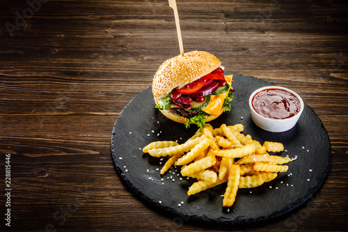 Tasty burger with chips served on black stone on wooden background