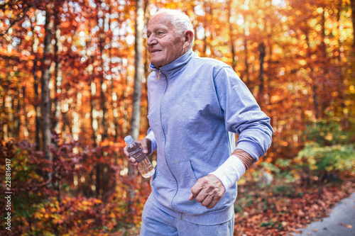 Senior runner in nature. Elderly sporty man running in forest during morning workout. Healthy and active lifestyle at any age concept