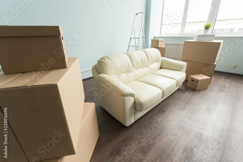 Relocation, moving and real estate concept- a new white sofa in empty room between an amount of boxes © satura_