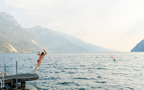 Young woman having fun and jumping into the water in lake lago di garda in Italy during holidays