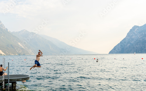 Young man having fun and jumping into the water in lake lago di garda in Italy during holidays