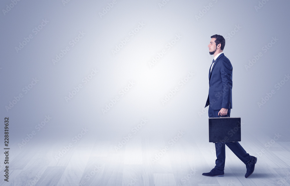 Successful businessman walking in front of an empty wall with briefcase on his hand
Successful businessman walking in front of an empty wall with briefcase on his hand