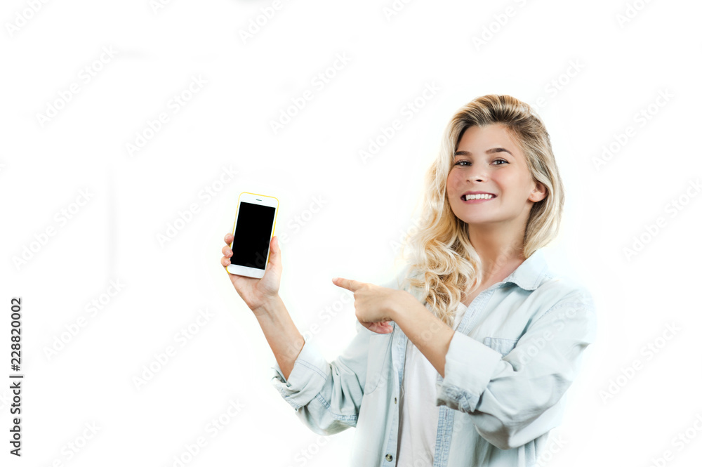 very beautiful young girl points to the smartphone, standing on a white isolated background. very beautiful young girl points to the smartphone, standing on a white isolated background.