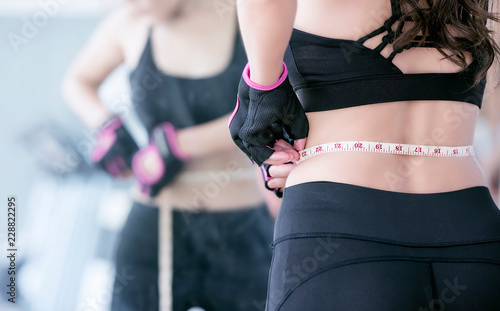 young woman in black fitness suite with a measuring tape.