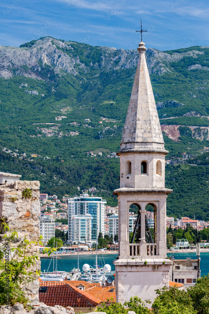 The bell tower of the church of Saint John with background of the new town of Budva, Montenegro and the blue waters of Adriatic Sea and the local port