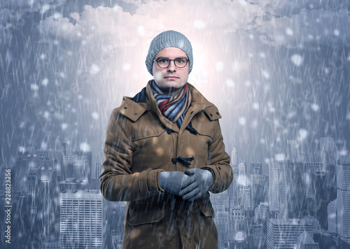 Young man freezing in warm clothing with city concept
