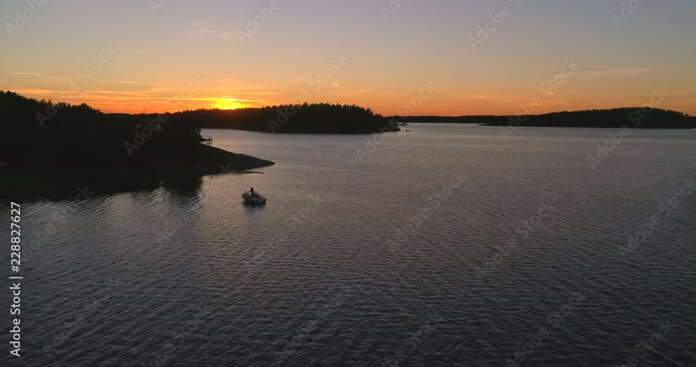 Aerial drone shot close to the sea bypassing a man fishing in the archipelago, between finnish islands, on the gulf of Finland, on a summer evening, in Sando, Hanko, Uusimaa, Finland
