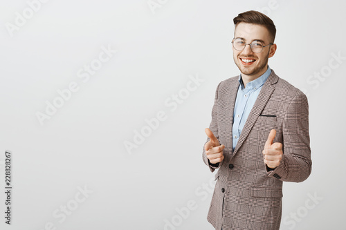 Hey nice job. Stylish happy and pleased caucasian businessman with stylish haircut and bristle in transparent glasses pointing at camera with finger guns smiling greeting or congratulating coworker