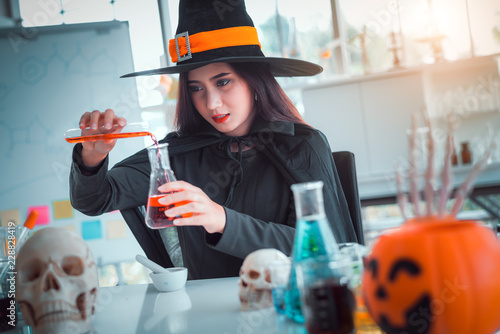 Attractive beautiful Asian woman dressed as a witch mixing poison or potion in test tube at modern laboratory, Halloween holidays. 