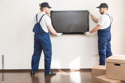 Delivery manremove the TV from the wall for moving to an apartment. professional worker of transportation, male loaders in overalls