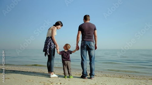 A happy family stands in front of the sea. Parents on the sea shore dandle their child. Slow motion