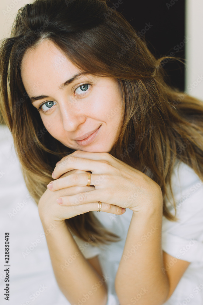 Portrait of young beautiful woman in white sitting on a bed at home Portrait of young beautiful woman in white sitting on a bed at home