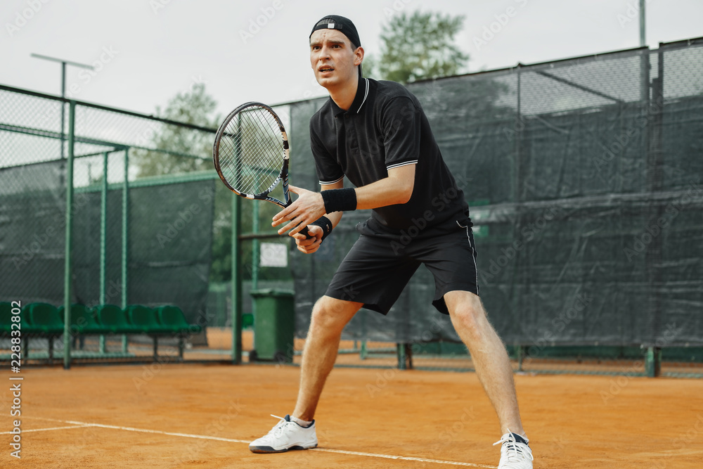 Distant plan of man holding tennis racket in both hands to straighten strike.