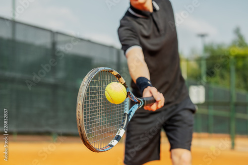 Close up of man playing tennis at court and beating the ball with a racket. © Akaberka