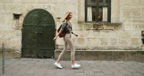 Caucasian young cheerful woman tourist walking the old town street, having fun and jumping. photo