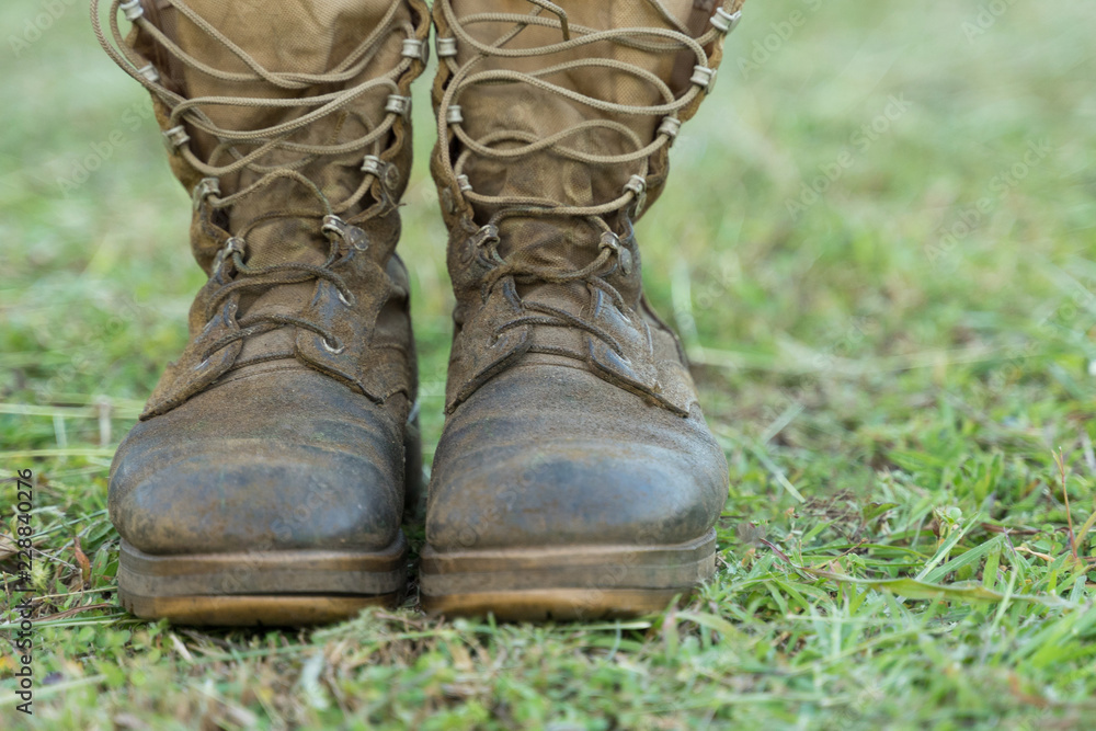Close up front view of a pair of muddy boots isolated on green grass  ground. Photos | Adobe Stock