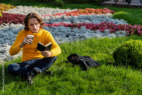 Foto The young man drinks coffee and reads the book in the park, he smiles, has a res