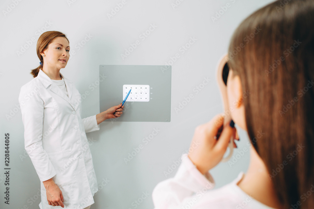 Fototapeta premium Caucasian optometrist checking girl's eyesight, pointing into special eye chart for checking vision.