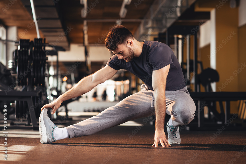 Handsome man doing warm up in the gym and stretch legs Handsome man doing warm up in the gym and stretch legs