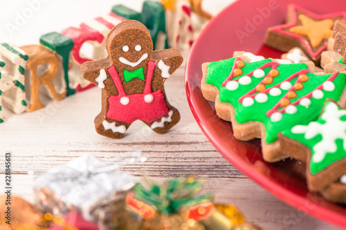 Tasty and cute baked Christmas cookies (gingerbread) with beautiful xmas decoration in red plate on light wooden table background, close up, copy space (text space)