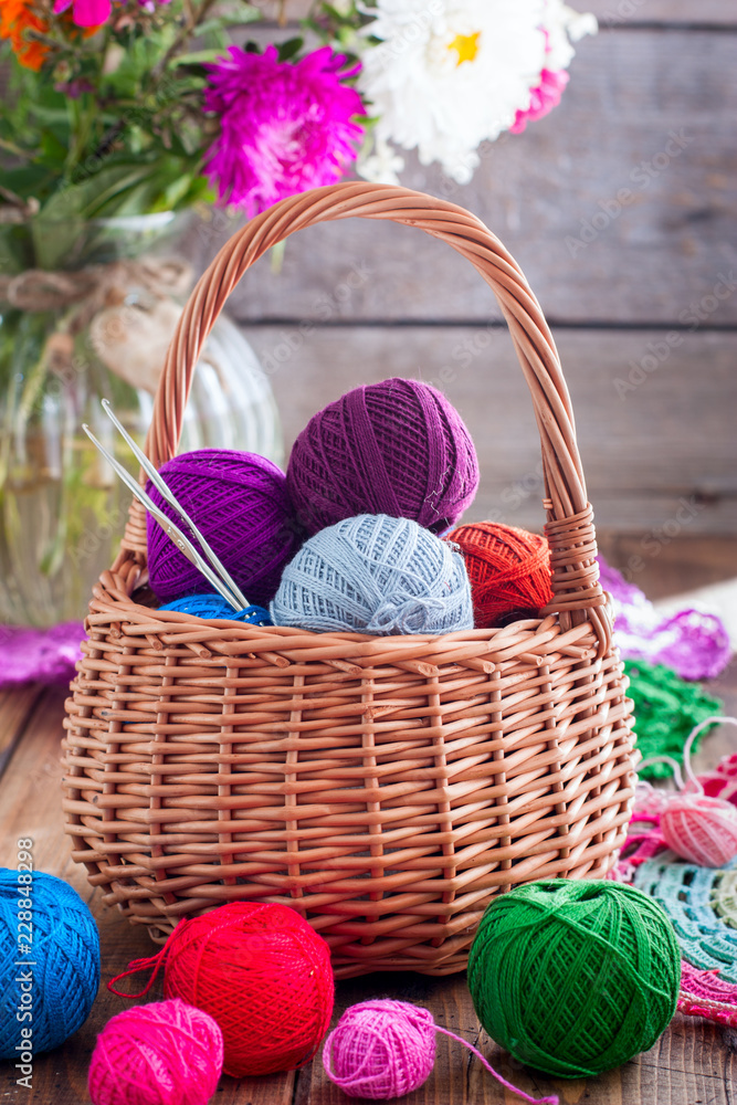 Multi-colored balls of cotton thread for crocheting in a wicker basket on a wooden table, selective focus