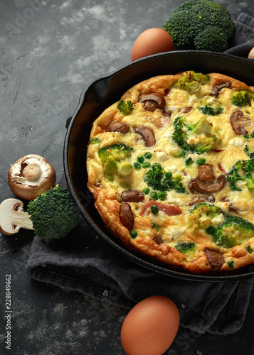 Homemade Frittata with mushrooms, broccoli, feta cheese, green peas and bacon on cast iron skillet