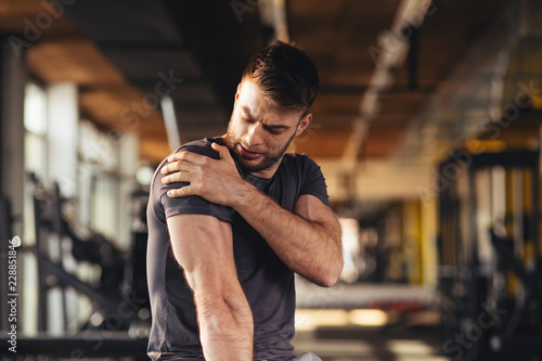 Handsome young man feeling the pain in shoulder at the gym photo