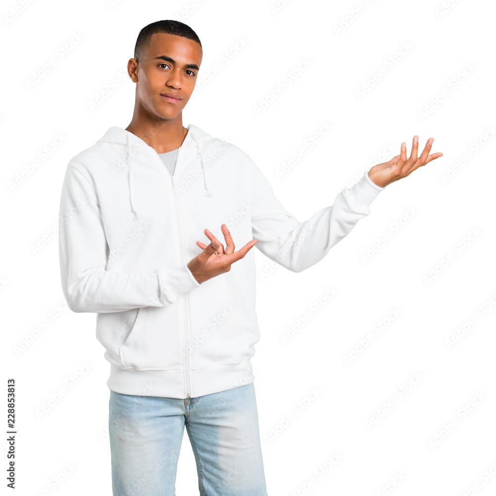 Dark-skinned young man with white sweatshirt extending hands to the side and smiling for presenting and inviting to come on isolated white background Dark-skinned young man with white sweatshirt extending hands to the side and smiling for presenting and inviting to come on isolated white background