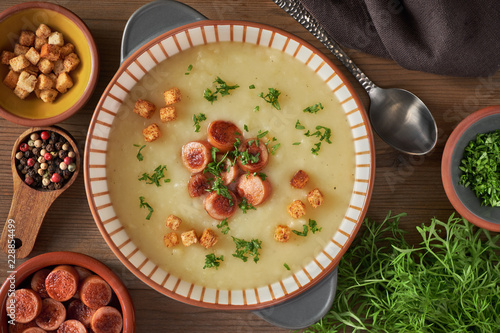 Flat lay of potato cream soup with croutons, fried vienna sausages and green coriander on dark