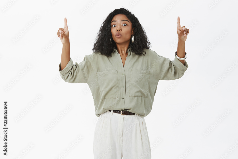 Wow you gotta see it. Portrait of impressed surprised and amused african american female in stylish boyfriend shirt and pants raising hands and pointing up folding lips from amazement and curiosity Wow you gotta see it. Portrait of impressed surprised and amused african american female in stylish boyfriend shirt and pants raising hands and pointing up folding lips from amazement and curiosity