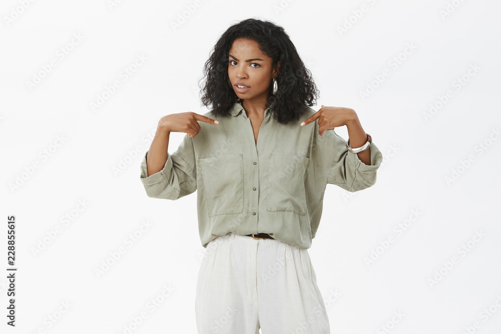 Stylish African-American woman pointing at herself with unsure expression being confused friend blamed het accused in making mistake raising eyebrow curiosly standing doubtful over white background Stylish African-American woman pointing at herself with unsure expression being confused friend blamed het accused in making mistake raising eyebrow curiosly standing doubtful over white background