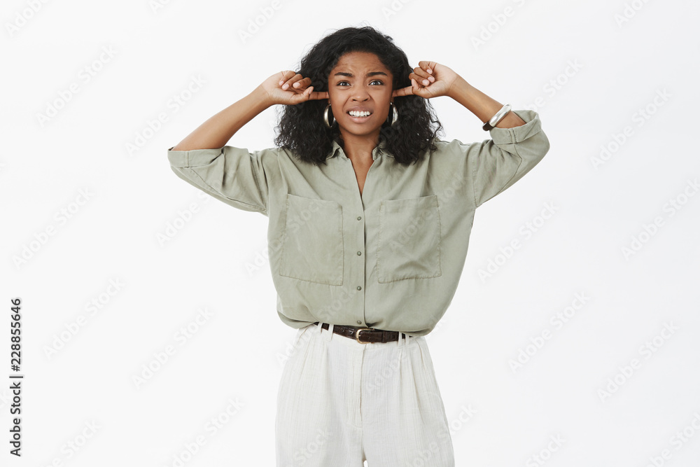 Hate living near club. Irritated displeased and pissed young attractive dark-skinned businesswoman feeling disturbed by loud annoying sound closing ears with index fingers clenching teeth from dislike Hate living near club. Irritated displeased and pissed young attractive dark-skinned businesswoman feeling disturbed by loud annoying sound closing ears with index fingers clenching teeth from dislike
