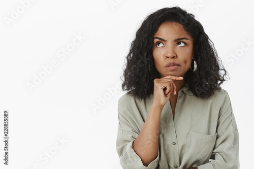 Hmm, maybe it work. Portrait of serious-looking thoughtful and smart businesswoman smirking and frowning looking up with hand on chin while thinking making up plan how make work of office better photo