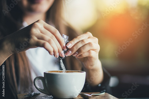 Female hand pours sugar into coffee. Sunlight background photo