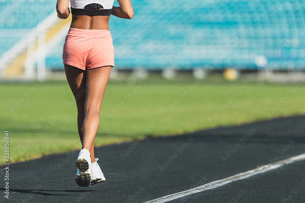 Back view of a fit sportswoman running a distance at the stadium