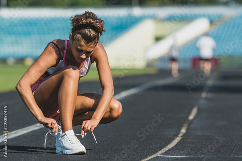 Close up of a young sportsgirl dressed in sportswear tying her shoelaces at the stadium