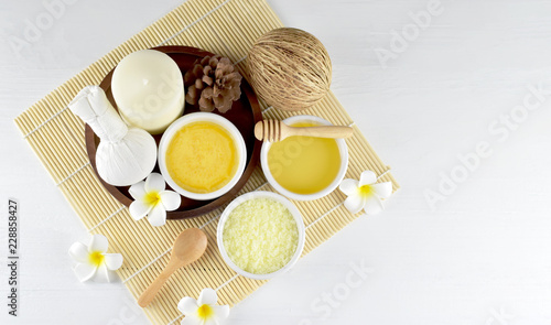 Homemade spa set (body and facial scrub, hair treatment oil, herbal compress, aroma candle and plumeria) in oriental style on white wood and old wood background, body and hair care concept