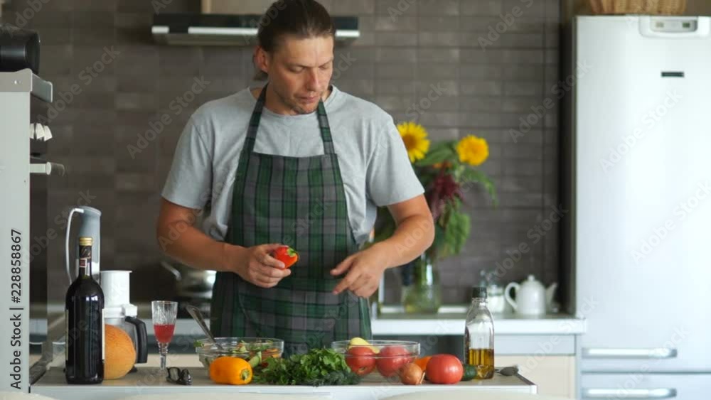 Happy man is cutting cucumbers for a salad while standing in his modern kitchen. He relaxed dancing. Healthy diet, vegetarianism, father's day Happy man is cutting cucumbers for a salad while standing in his modern kitchen. He relaxed dancing. Healthy diet, vegetarianism, father's day