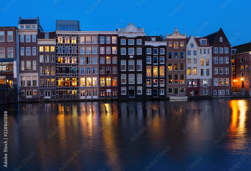 Historical houses facades over canal with reflections illuminated at night, Amsterdam, Netherlands