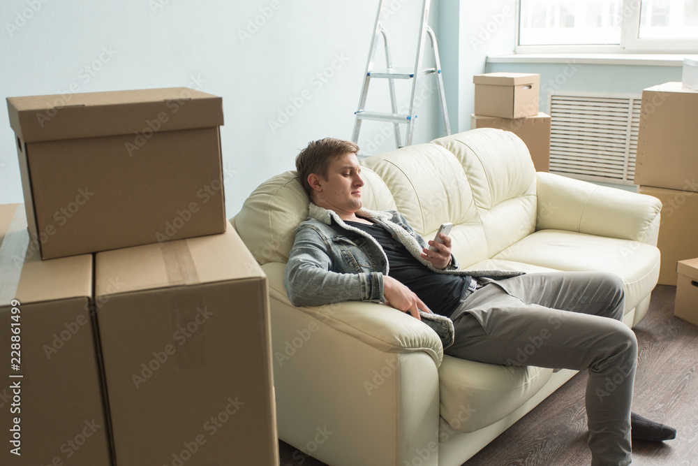 Moving process,real estate and new home concept - tired guy sits on the sofa in the empty room Moving process,real estate and new home concept - tired guy sits on the sofa in the empty room