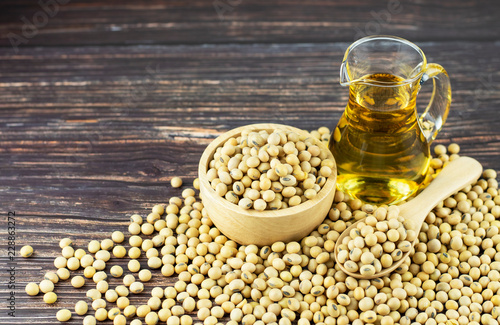 Closeup of soybean oil (vegetable oil) in a glass jug, uncooked soy beans in an a wooden bowl and spoon on old wooden background with copy space for text, healthy diet and cooking ingredients