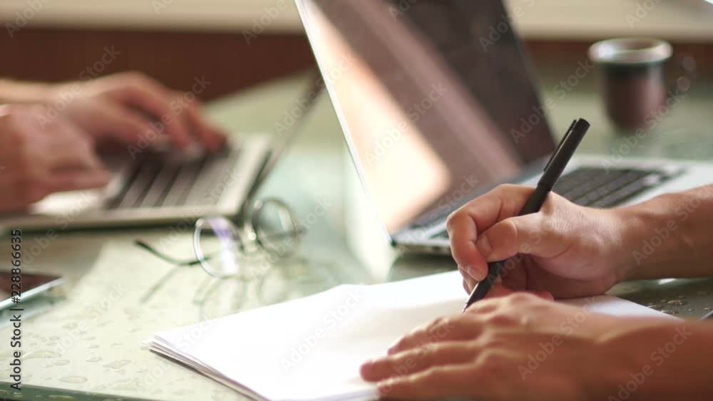 Two businessmen at work. Close-up hands and laptops. One man draws a scheme, drawing on paper, training colleagues, transfer of experience, coaching Two businessmen at work. Close-up hands and laptops. One man draws a scheme, drawing on paper, training colleagues, transfer of experience, coaching