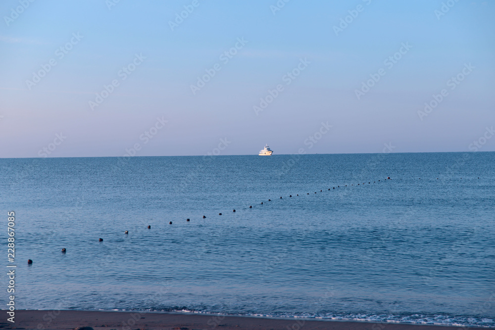 The image on the horizon of the white ship, the blue sea and blue sky. The background is natural. Cropped shot, isolated, close-up, blurred