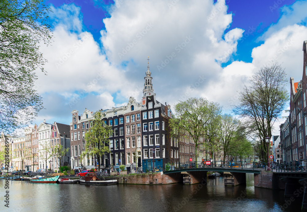Facades of old historic Houses over canal water with spring green trees, Amsterdam, Netherlands