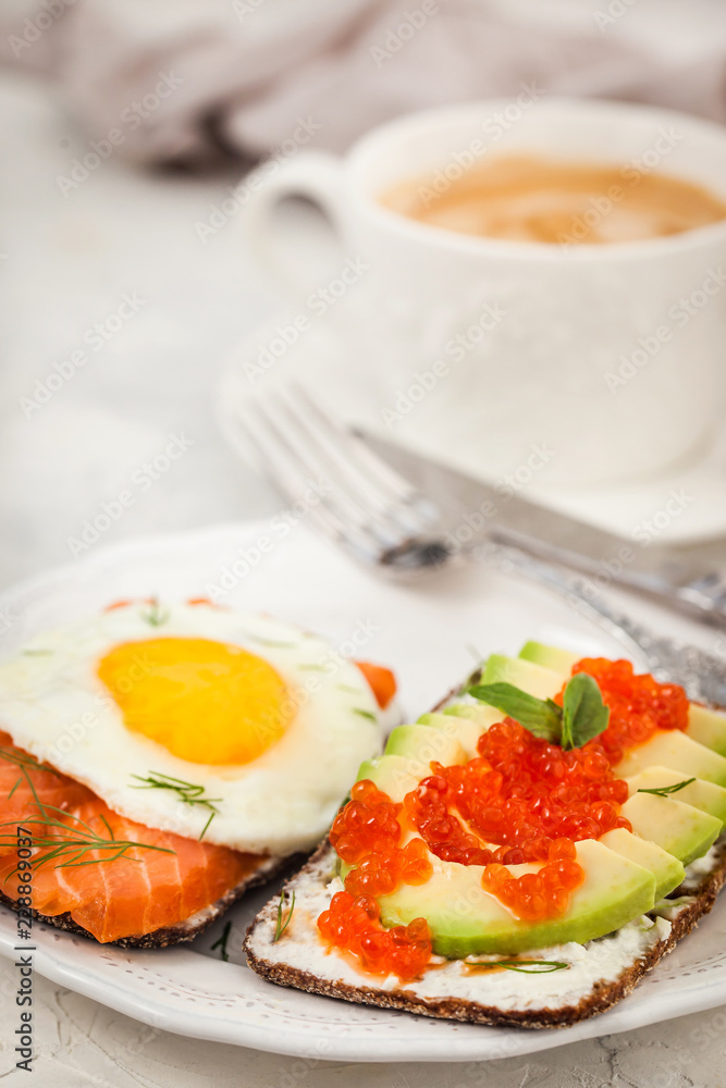 Avocado and red caviar, smoked salmon and fried egg rye toasts for breakfast, close up